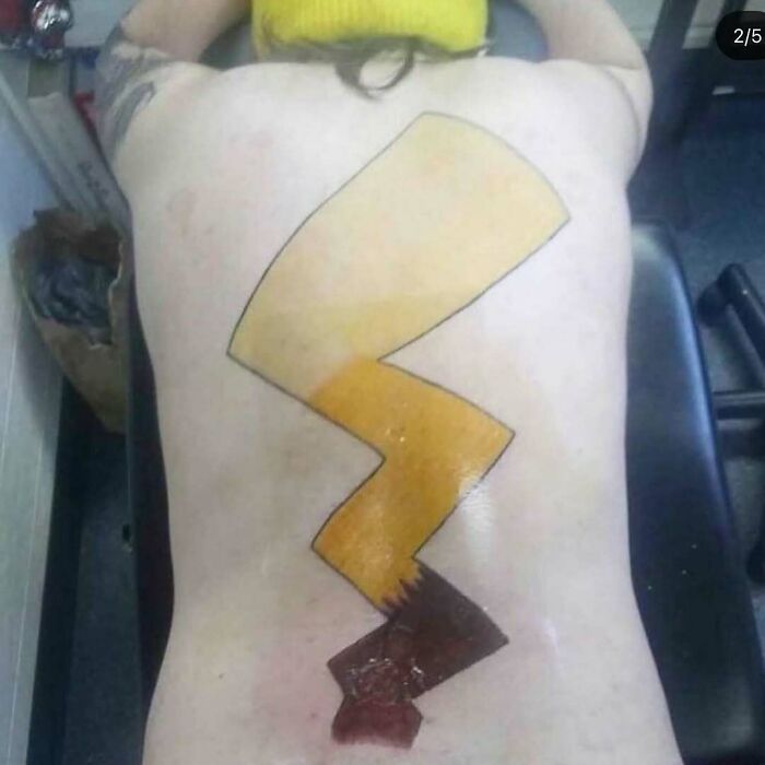 Person lying face down showing a bizarre tattoo of a large lightning bolt on their back, showcasing strange tattoo choices.