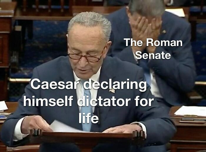 Man in suit sitting at desk with papers and glasses, meme about Caesar and the Roman Senate, history memes concept.