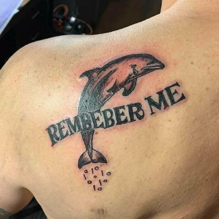 Tattoo of a dolphin combined with the words remember me featuring a misspelled bizarre choice on a person's back.