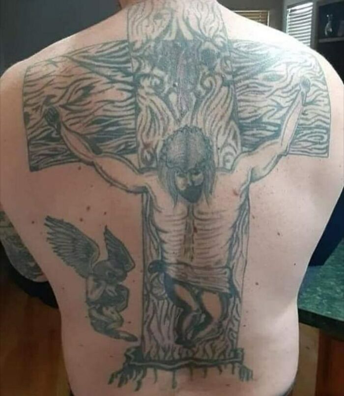 Large back tattoo of a crucifixion scene with an angel in a bizarre tattoo choice on bare skin.