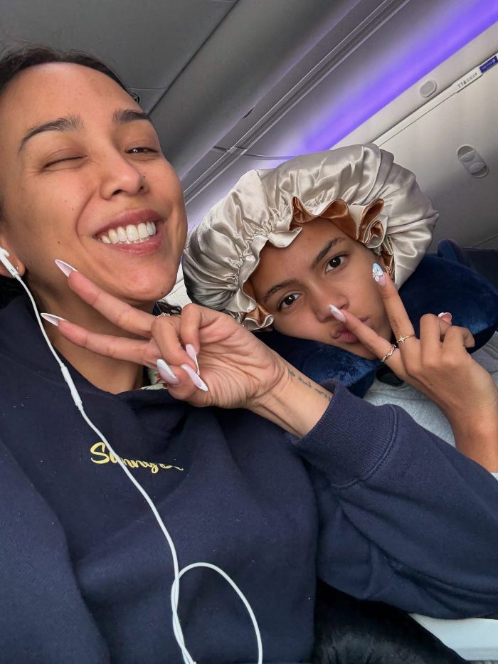 Two young women on a plane making peace signs, representing an Aussie influencer in the US amid cost of living complaints.