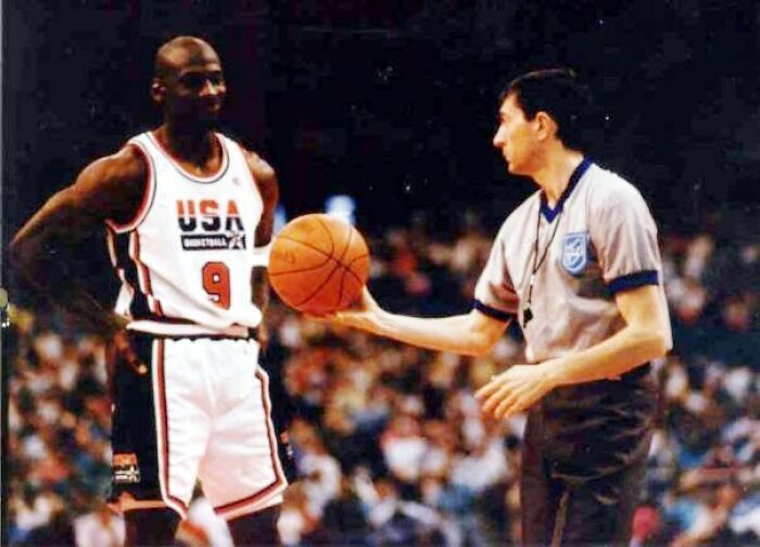 Basketball player in USA jersey interacts with referee during a game, illustrating teamwork and sportsmanship.