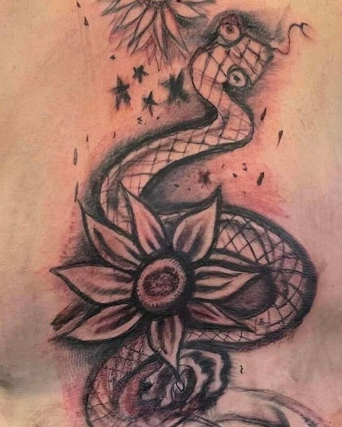 Abstract snake and flower tattoo with unusual design elements in black ink on skin, showcasing bizarre tattoo choices.