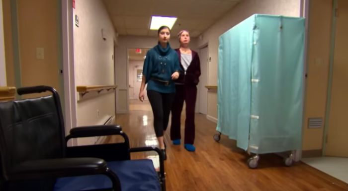 Woman walking with assistant in hospital corridor 16 years after face transplant from chimpanzee attack