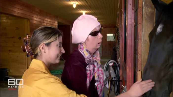 Woman whose face was torn apart by chimpanzee touching a horse with assistance, revealing her appearance after face transplant.