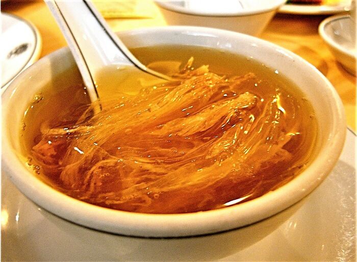 Bowl of edible bird’s nest soup, one of the surprising foods banned in the USA, served with a white spoon.