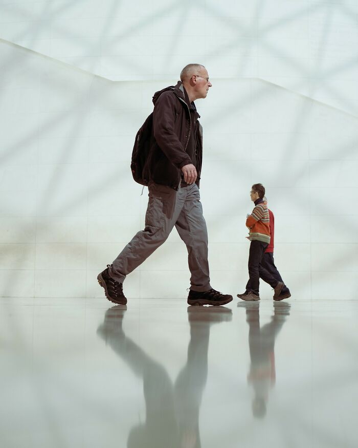 Man and two children walking inside a minimalist space with reflections on the floor, showcasing stunning color photography.