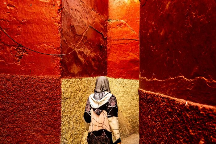 Person walking through narrow alley with vibrant red and orange walls, showcasing stunning color photography from 1839 awards.
