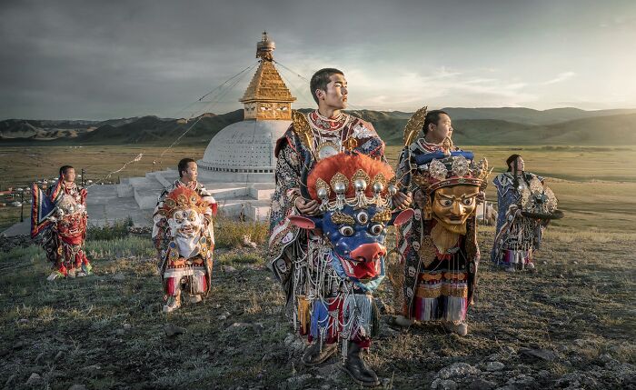 Color photography winners showcasing traditional costumes and masks in a scenic landscape near a large stupa monument.
