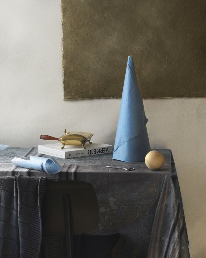 Still life with blue paper cone, brass teapot, book, and wooden sphere on a textured table featuring color photography elements.