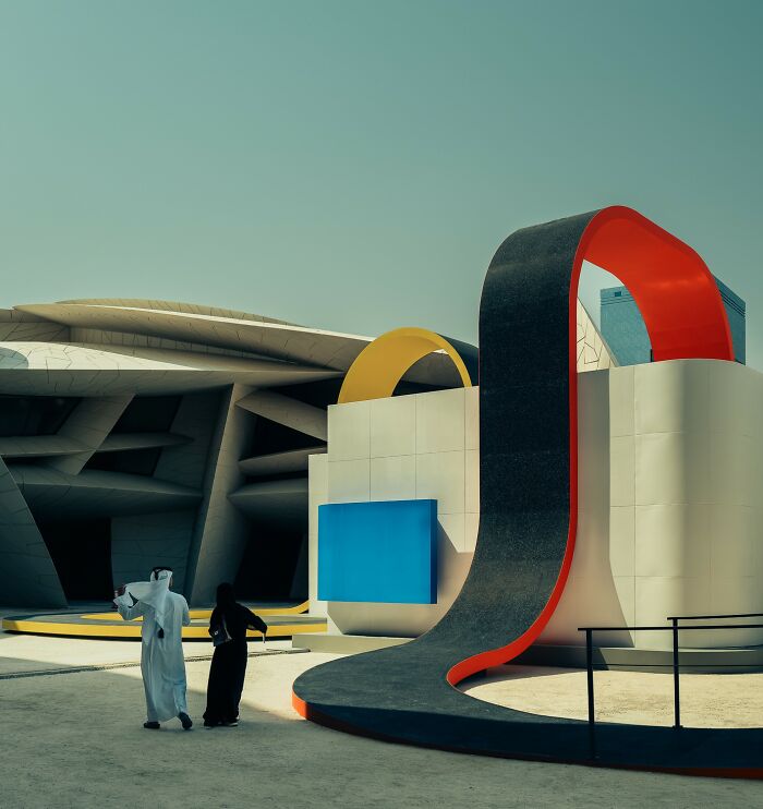People walking near modern abstract colorful sculpture outdoors in bright sunlight, showcasing stunning color photography.