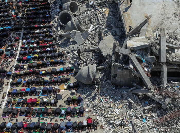 Aerial view of people praying next to rubble and destruction captured in stunning color photography.