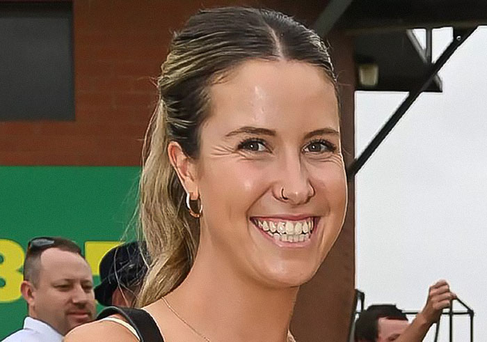 Young woman with a ponytail smiling outdoors, related to news about woman who set male friend on fire over misogynistic comment.