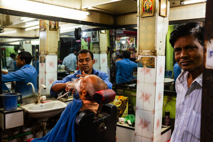 Barber shaving an elderly man's beard in a candid street moment captured by a photographer traveling the world.