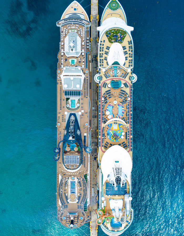 Aerial view of two cruise ships docked side by side at a pier in clear blue ocean water.