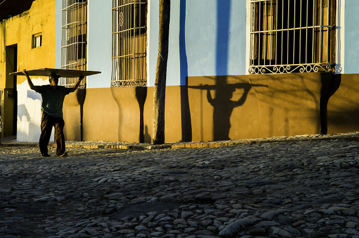 Man carrying a large item on his head walking on cobblestone street in cinematic photo by Adriana Ferrarese