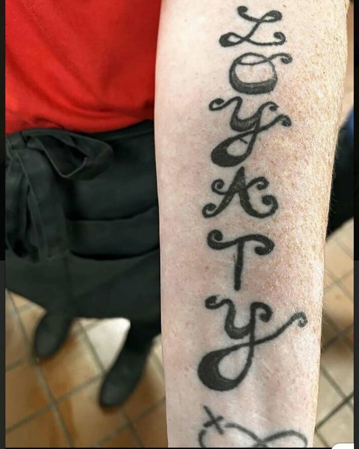 Tattoo on forearm with bizarre lettering spelling a word vertically, showcasing a strange tattoo choice.