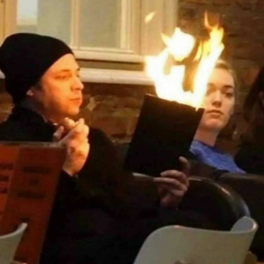Person nonchalantly holding a burning book indoors, one of the bizarre hilarious pics causing a double take moment.