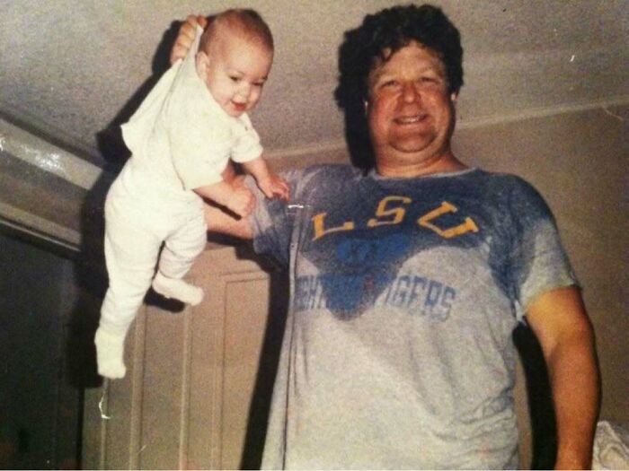 Man smiling and holding baby by one arm indoors, illustrating learning weird things about history on Instagram.