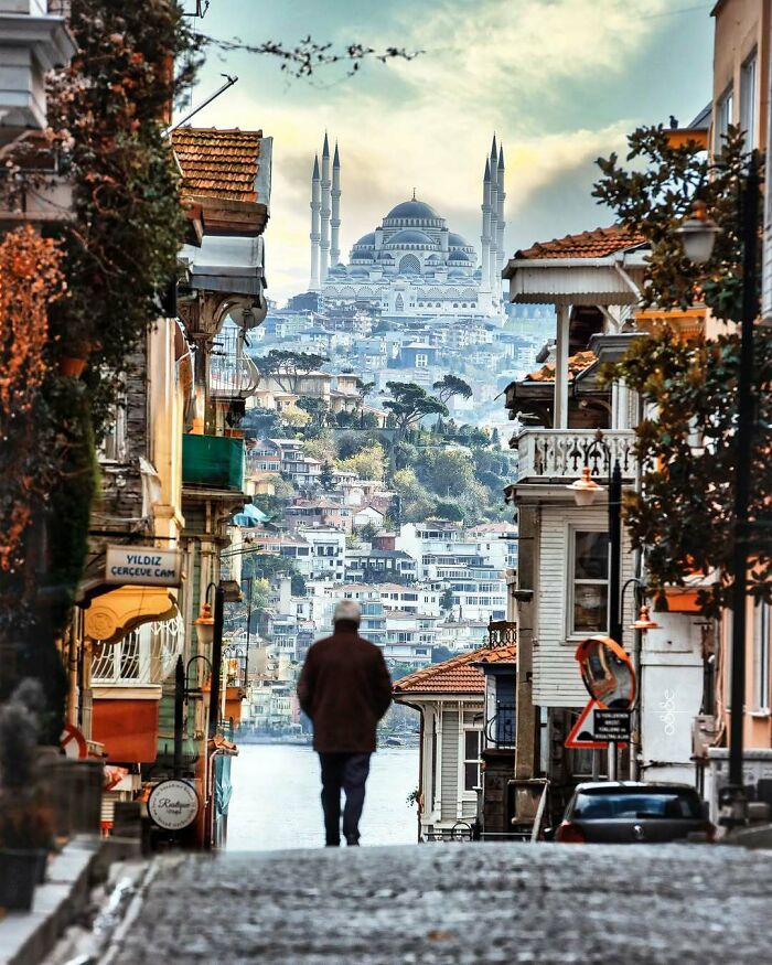 Man walking down a narrow street with famous landmark mosque visible in the distance from an unexpected angle.