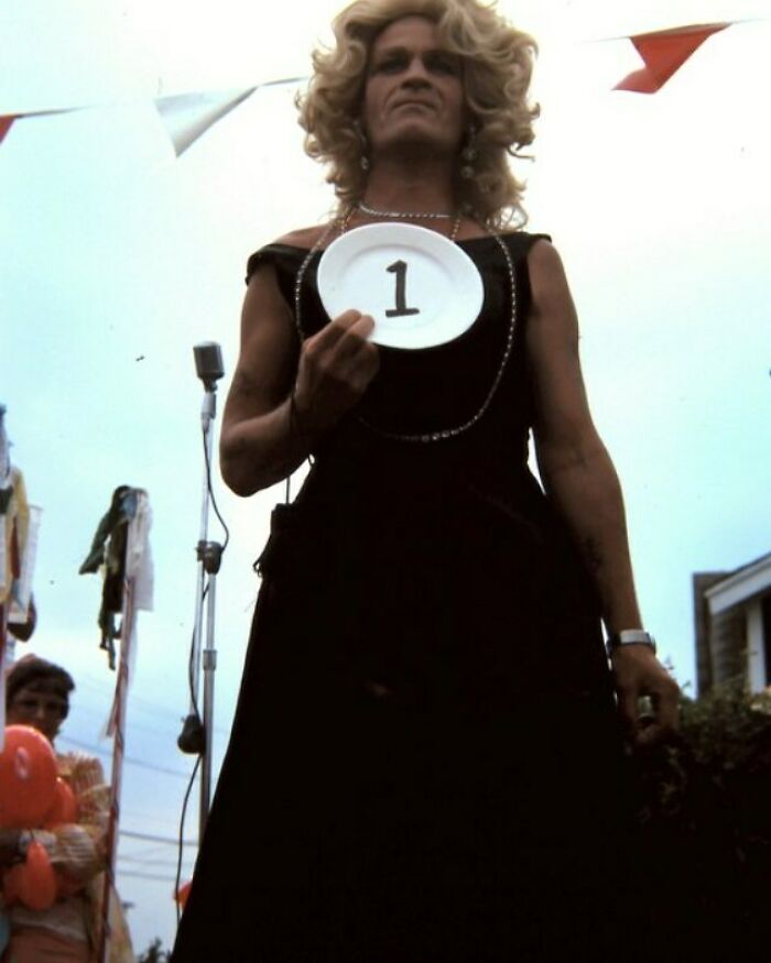 Person in vintage costume holding a plate with number one at a confusing historical event outdoors.