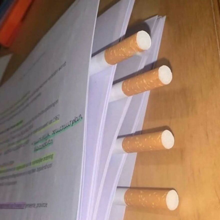 Stack of papers held together with cigarettes used as unusual paper clips in a bizarre yet hilarious pic.