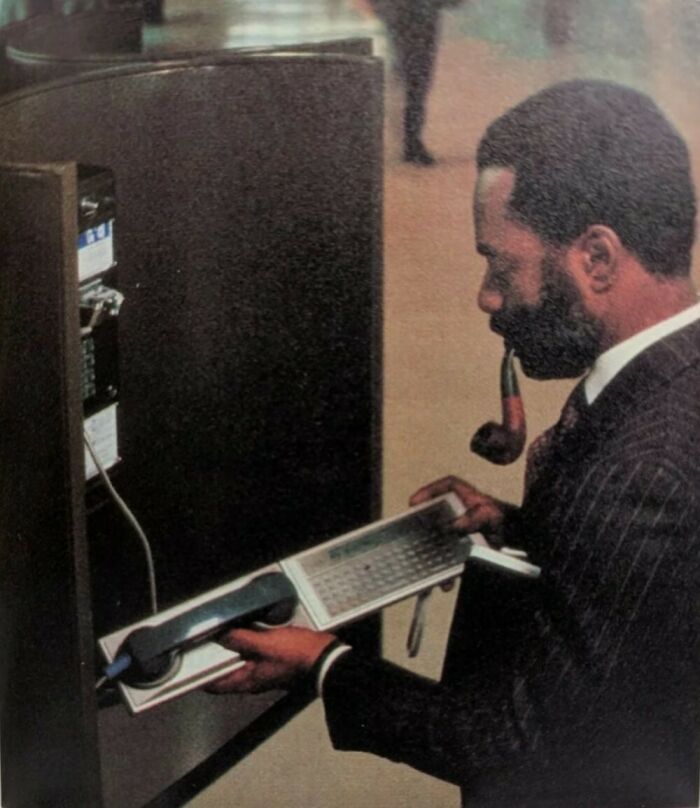Man with pipe using a vintage telephone with an attached keyboard, showcasing old technology that looks confusing now.