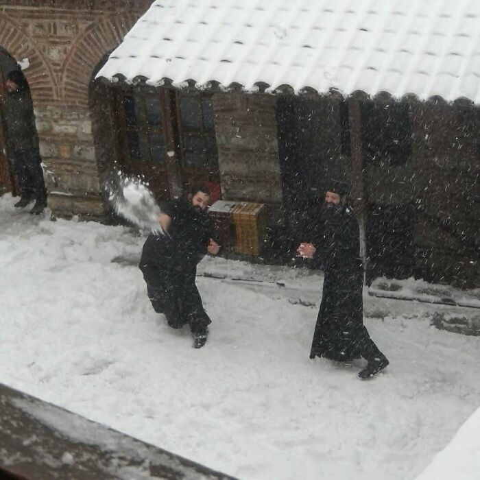 Two men in dark clothing having a snowball fight outside a snow-covered building, showcasing nature and random fun facts.