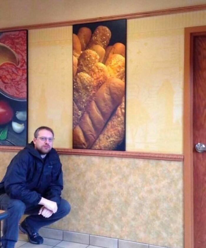 Man squatting in a room with wall art of bread, a bizarre image under nature, animals and random fun facts category.
