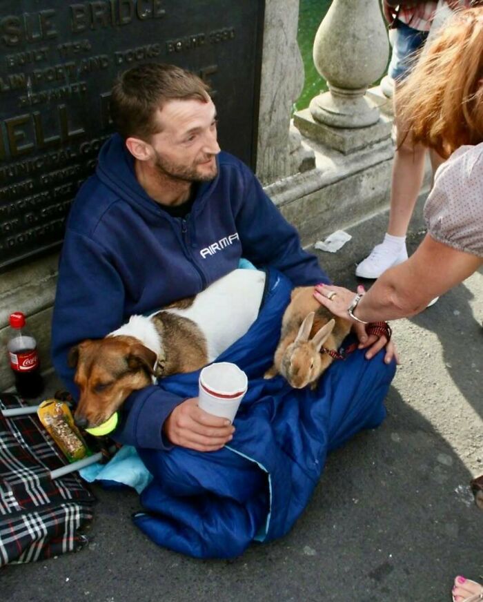 Man sitting on sidewalk with a dog and rabbit in a sleeping bag, showcasing nature, animals, and random fun facts.