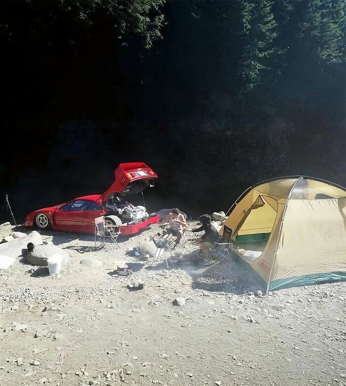 Camping setup with a red sports car and tent on rocky terrain, showing a unique nature and animals outdoor scene.