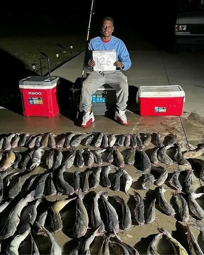 Young man displaying a large catch of catfish on driveway at night, showcasing nature and animals in a unique setting.