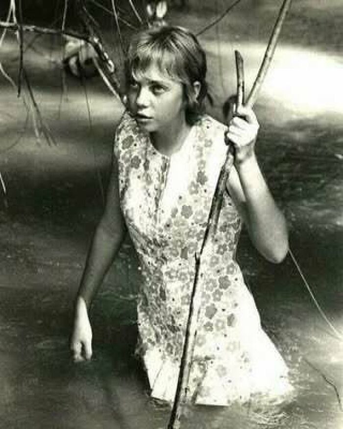 Young woman wading through water holding a stick, vintage black and white photo for learning weird things about history.