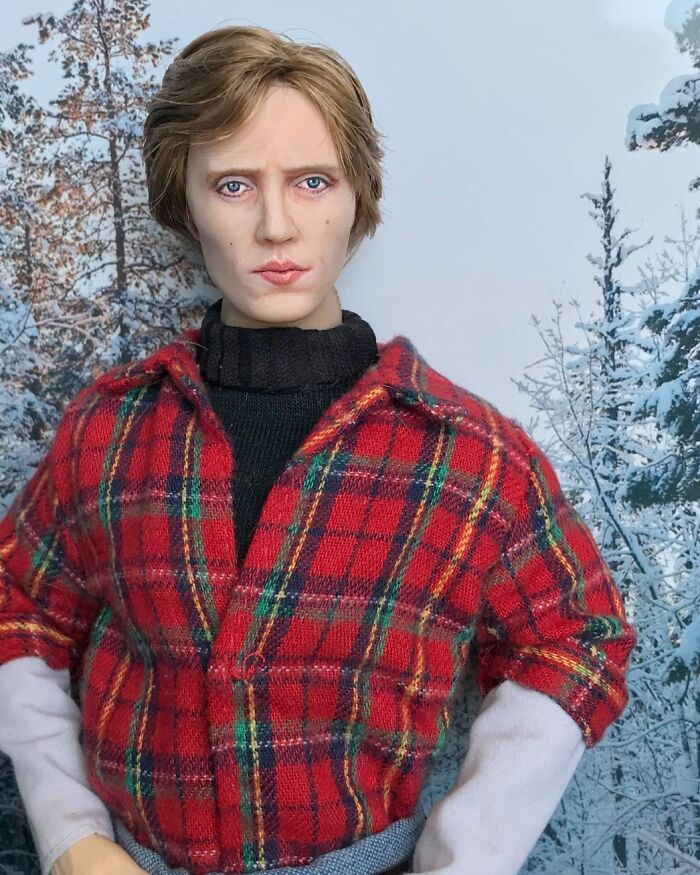 Detailed vintage-style doll wearing a red plaid shirt and black turtleneck against a snowy forest background.