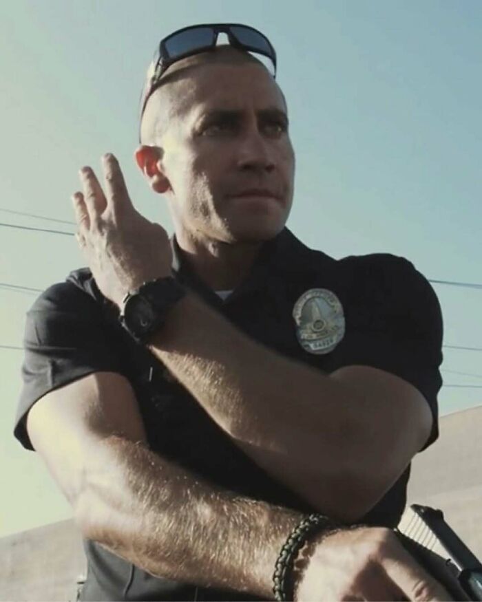 Policeman adjusting sunglasses on his head outdoors with strong sunlight, unrelated to nature, animals, or fun facts.
