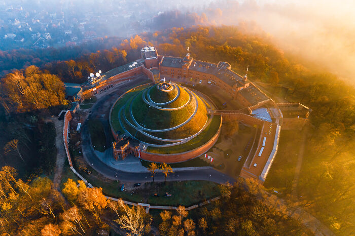 Aerial view of a famous landmark featuring circular terraces and walls surrounded by autumn trees and fog.