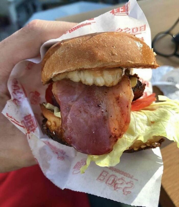 Close-up of a bacon burger held in hand, illustrating a bizarre and fun food fact related to nature and animals.