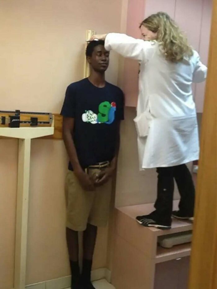 A person wearing beige shorts and a black shirt being measured for height by a medical professional in a clinical setting.