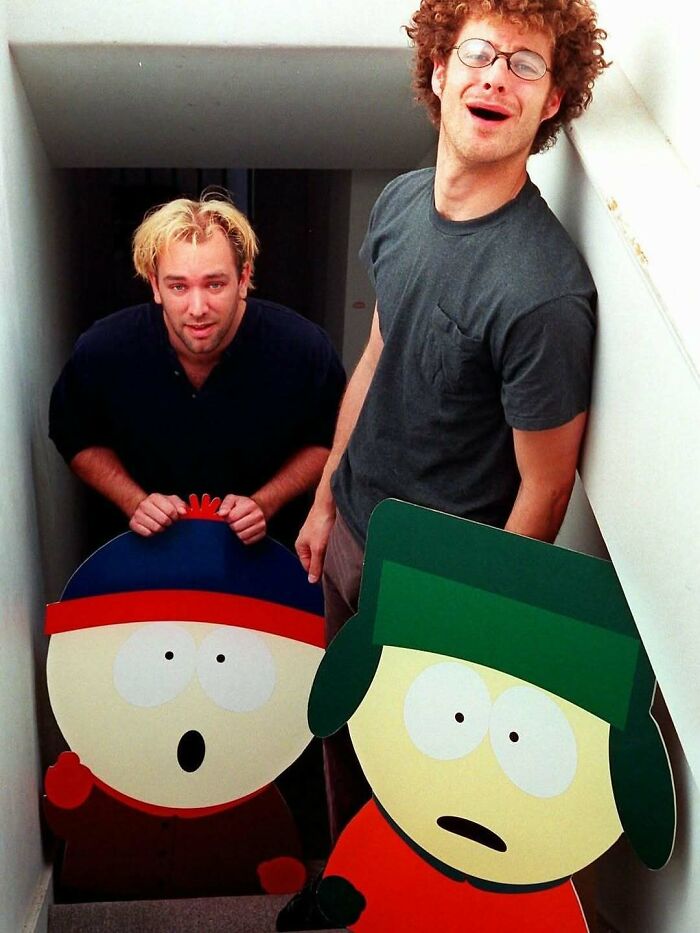 Two men with cardboard cutouts of animated characters in a narrow stairwell, related to nature, animals, and fun facts.