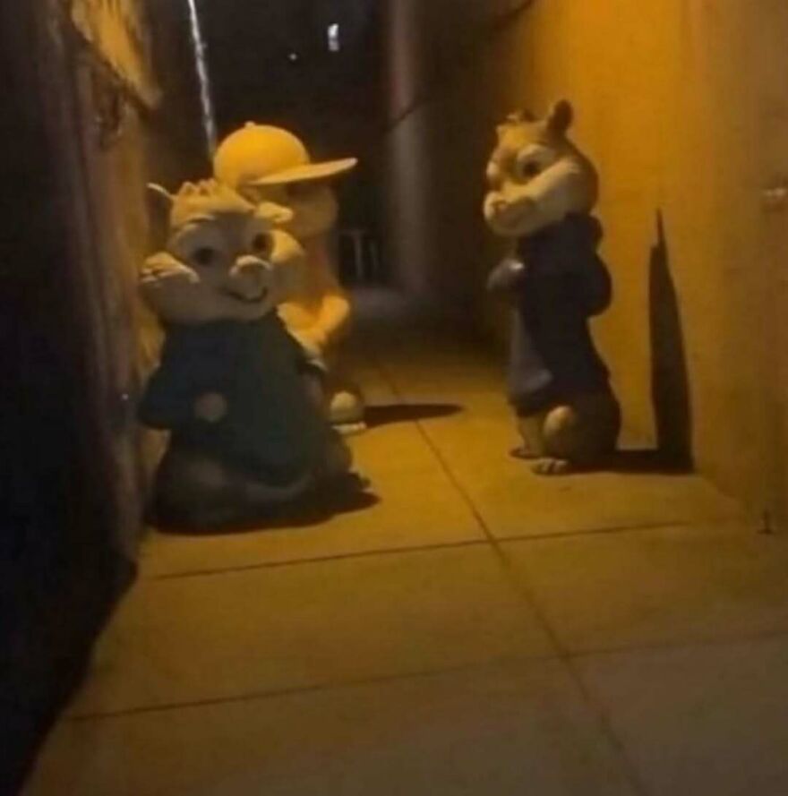 Three chipmunk statues in an alleyway at night with yellow lighting, creating a bizarre yet hilarious scene.