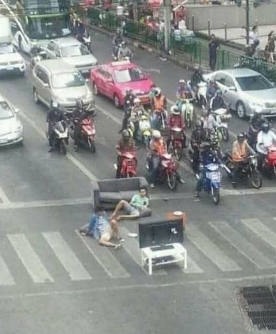 Two men lounging on a couch and watching TV in the middle of a busy street in a bizarre yet hilarious pic.