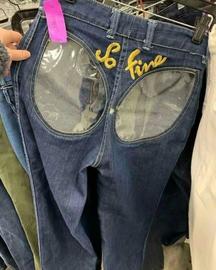 Denim jeans with transparent back pockets and embroidered text, displayed among cool secondhand finds in a thrift store.