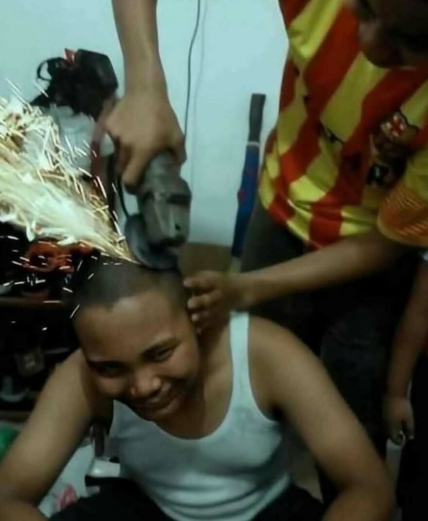 Man smiling while another uses a grinder on his head, creating sparks in a bizarre yet hilarious moment.