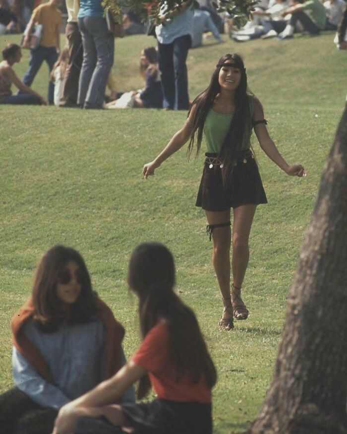 Young woman enjoying a sunny day in a park, surrounded by people, capturing a moment linked to weird things about history.
