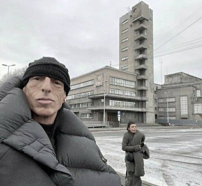 Two people wearing oversized padded jackets standing outside an industrial building in cold weather, nature animals.