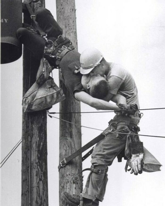 Two utility workers high on a pole sharing a life-saving mouth-to-mouth rescue in a historic moment.