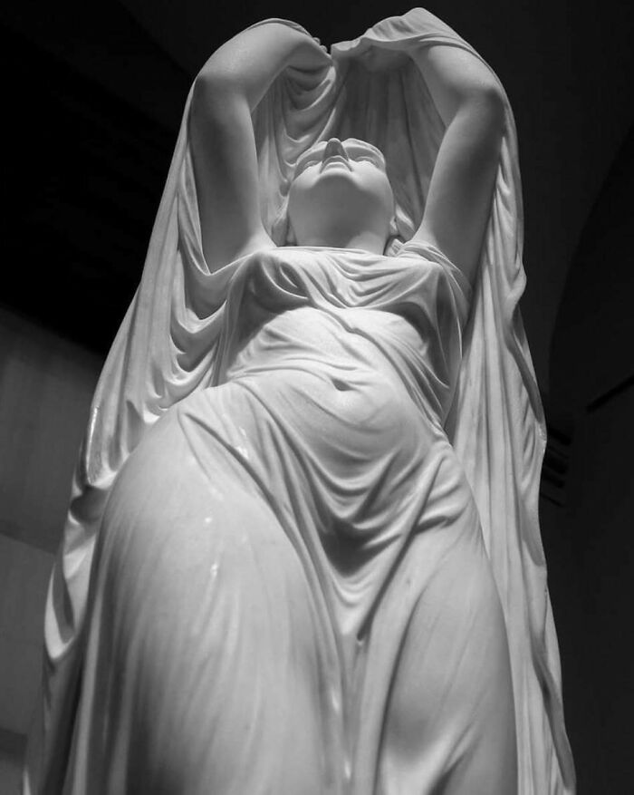 Marble statue of a draped woman with arms raised, representing weird things about history in art form.