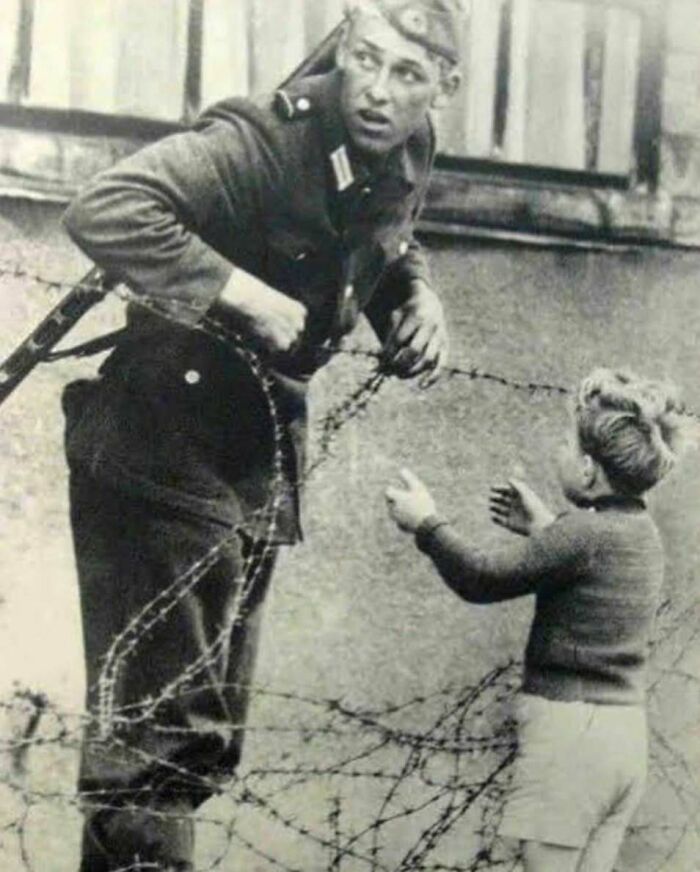 Black and white historic photo of soldier communicating with a child through barbed wire fence, learn weird things about history.