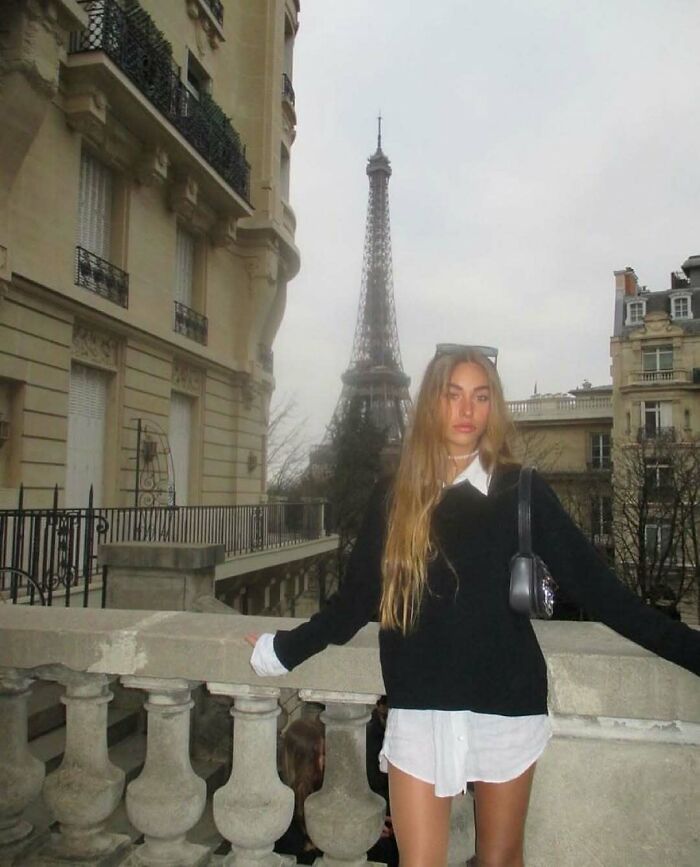 Young woman posing near a Parisian balcony with the Eiffel Tower in the background, showcasing nature and travel vibes.