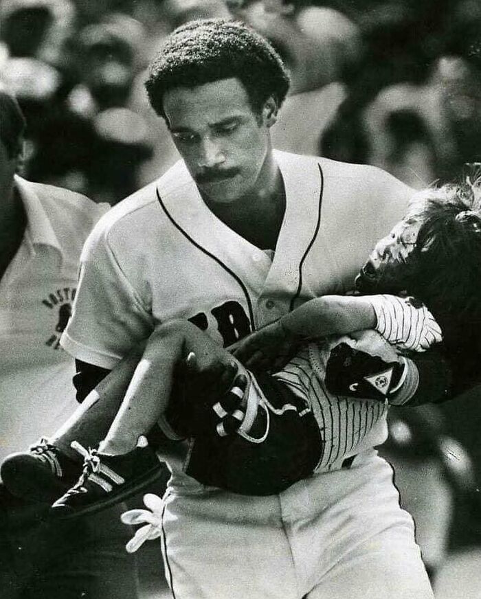 Black and white photo of a baseball player carrying an injured child, illustrating weird things about history.